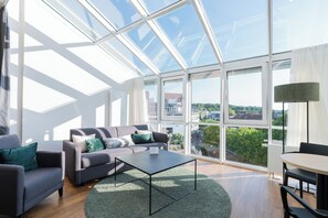 A modern living room with a glass ceiling, a grey sofa, a coffee table, and a view of the city. - Hotel Arkadia (Friedrichsdorf)