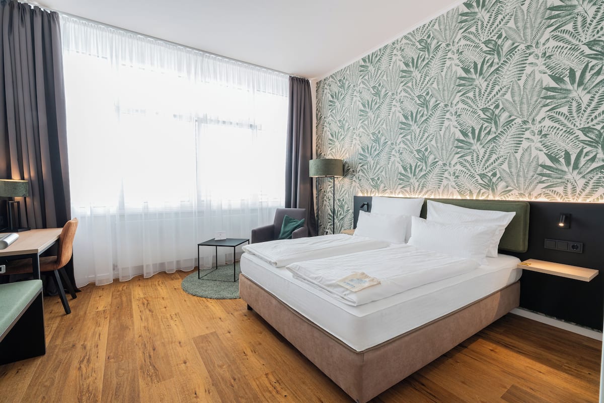 A hotel room with a bed, desk, chair, and a view of the city.