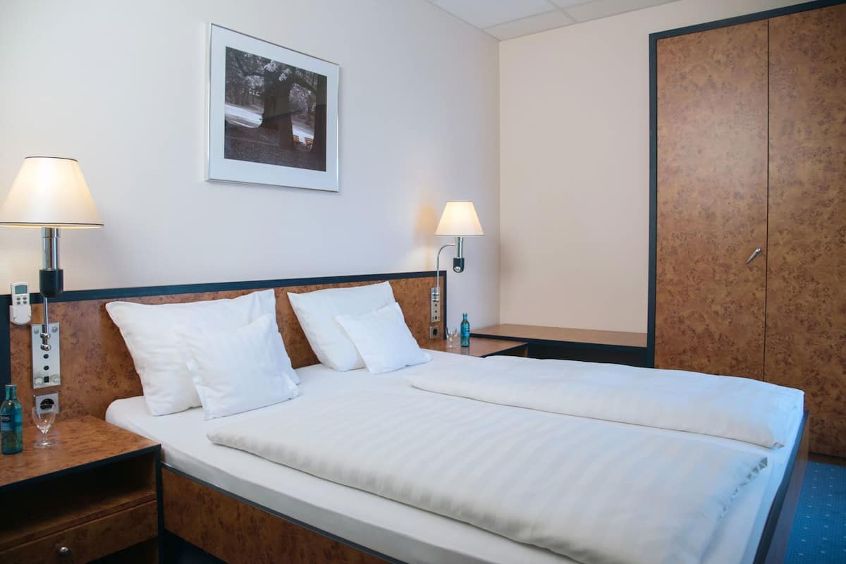 A hotel room with a bed, two bedside lamps, a nightstand, a wall-mounted picture, and a wardrobe.