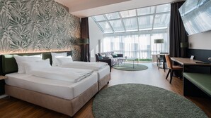Een hotelkamer met een groot bed, een bureau, een bank en uitzicht op de stad door grote ramen.