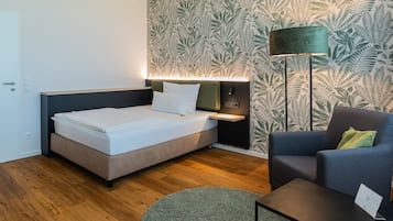 A modern hotel room with a bed, a nightstand, a lamp, a chair, and a small table.