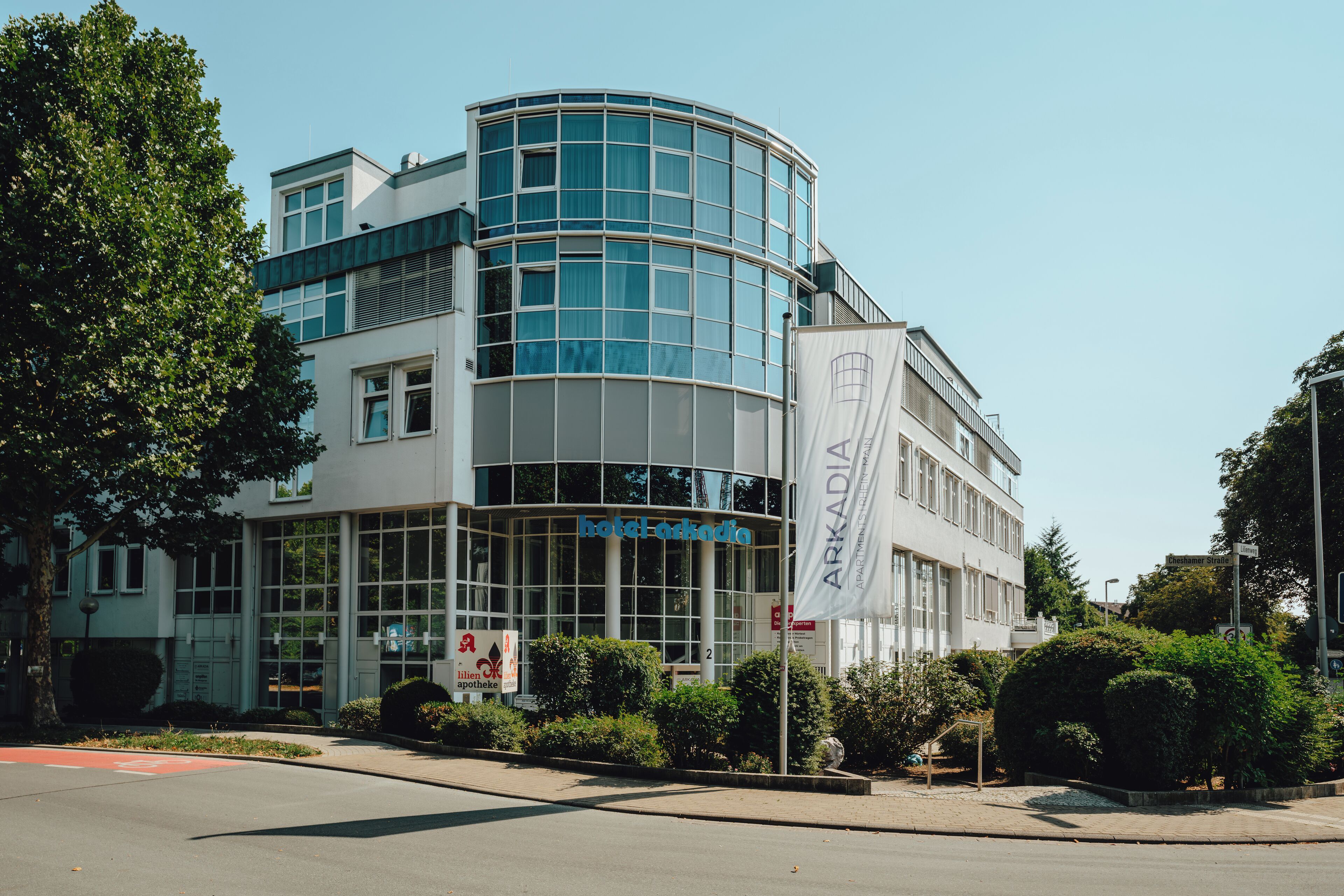 Un hôtel moderne doté d’une façade en verre incurvée, d’une entrée imposante et d’un mât pour drapeau.
