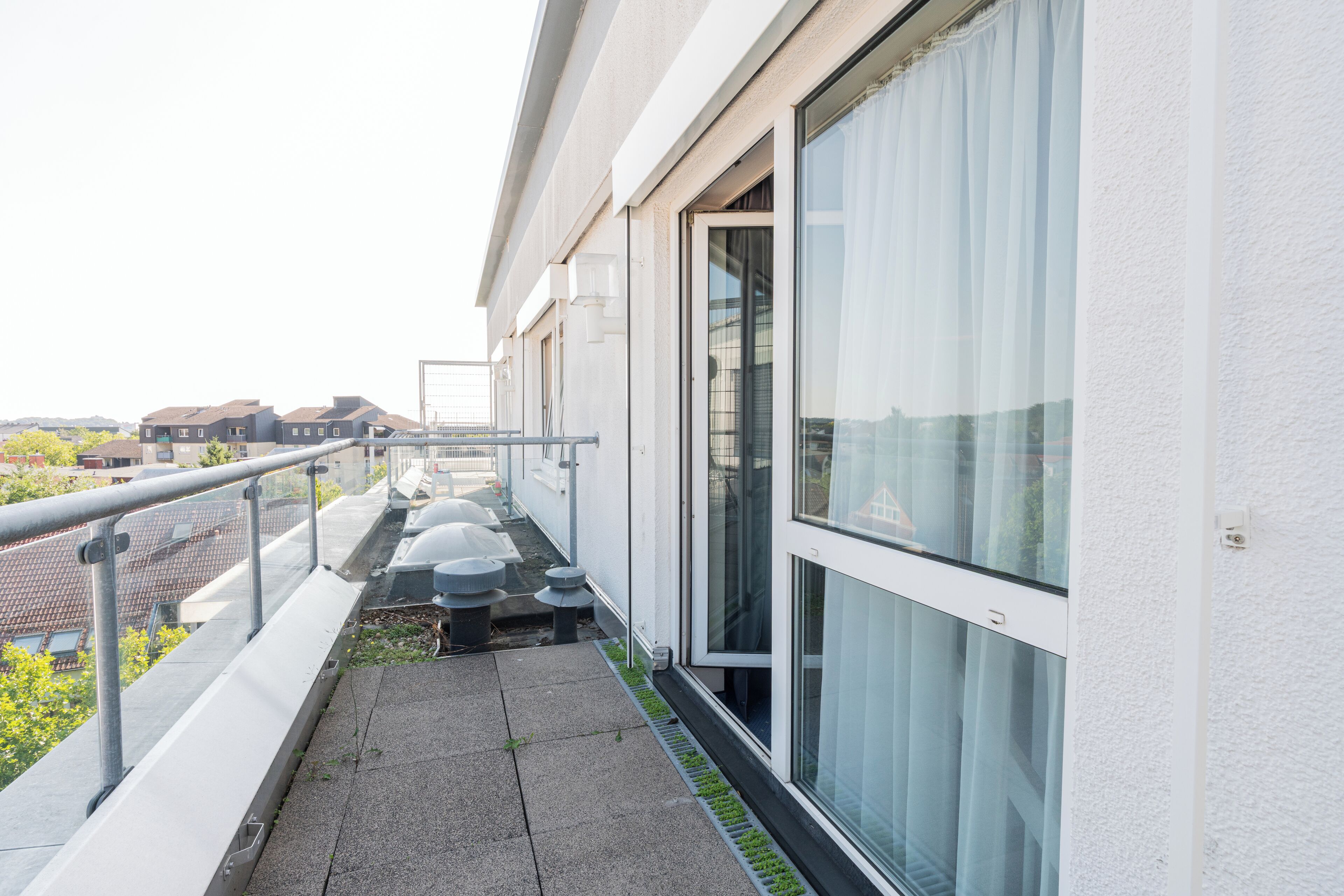 Un bâtiment moderne doté de grandes fenêtres, d’un balcon avec une rambarde en métal et d’un chemin piétonnier pavé.