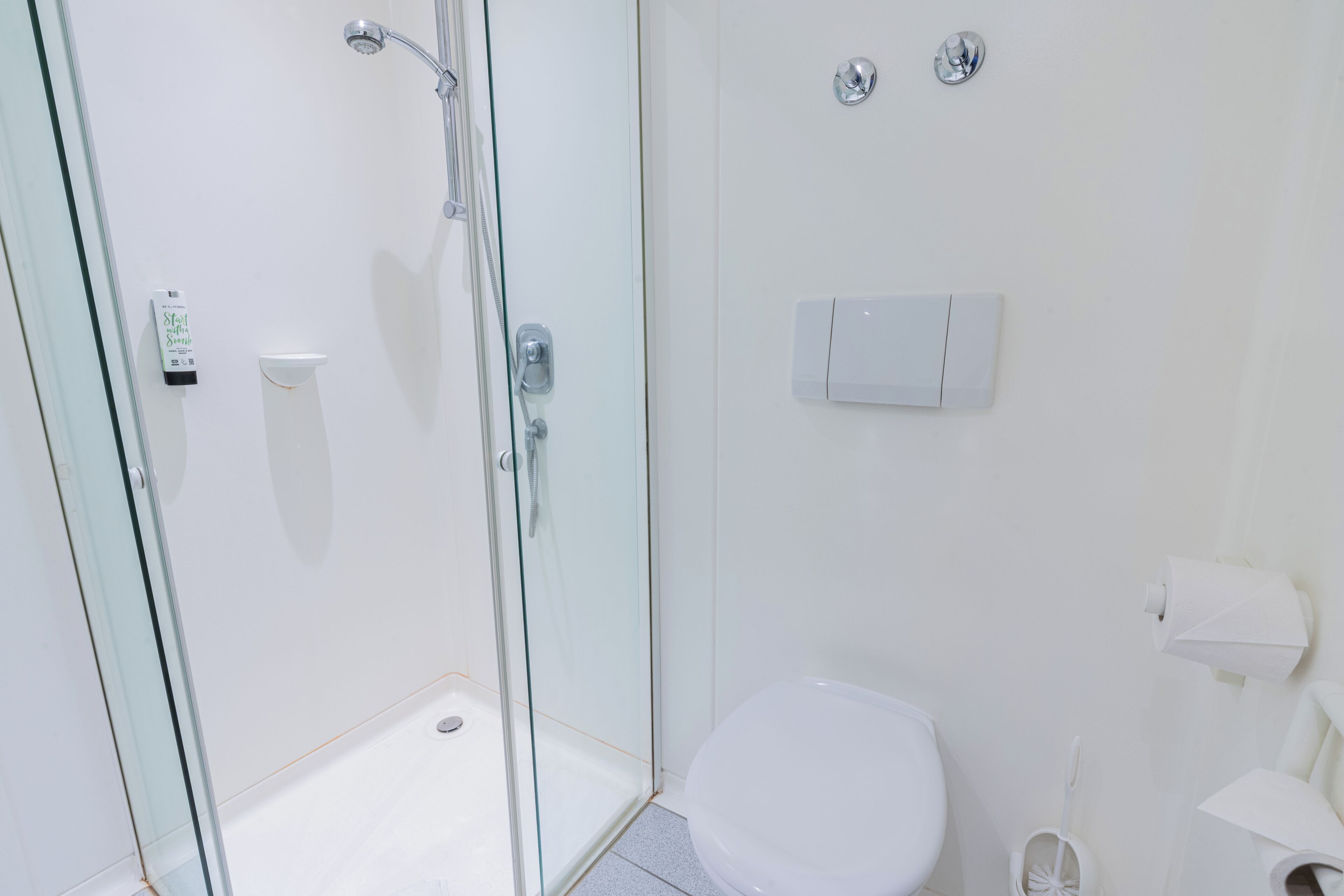 Un baño moderno con cabina de ducha de vidrio, inodoro y dispensador de papel higiénico adherido a la pared.