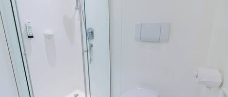 Un baño moderno con cabina de ducha de vidrio, inodoro y dispensador de papel higiénico adherido a la pared.