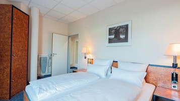 Une chambre d’hôtel avec un grand lit, une armoire en bois, une salle de bain avec une serviette suspendue, un tableau encadré au mur et une table de chevet avec une lampe.