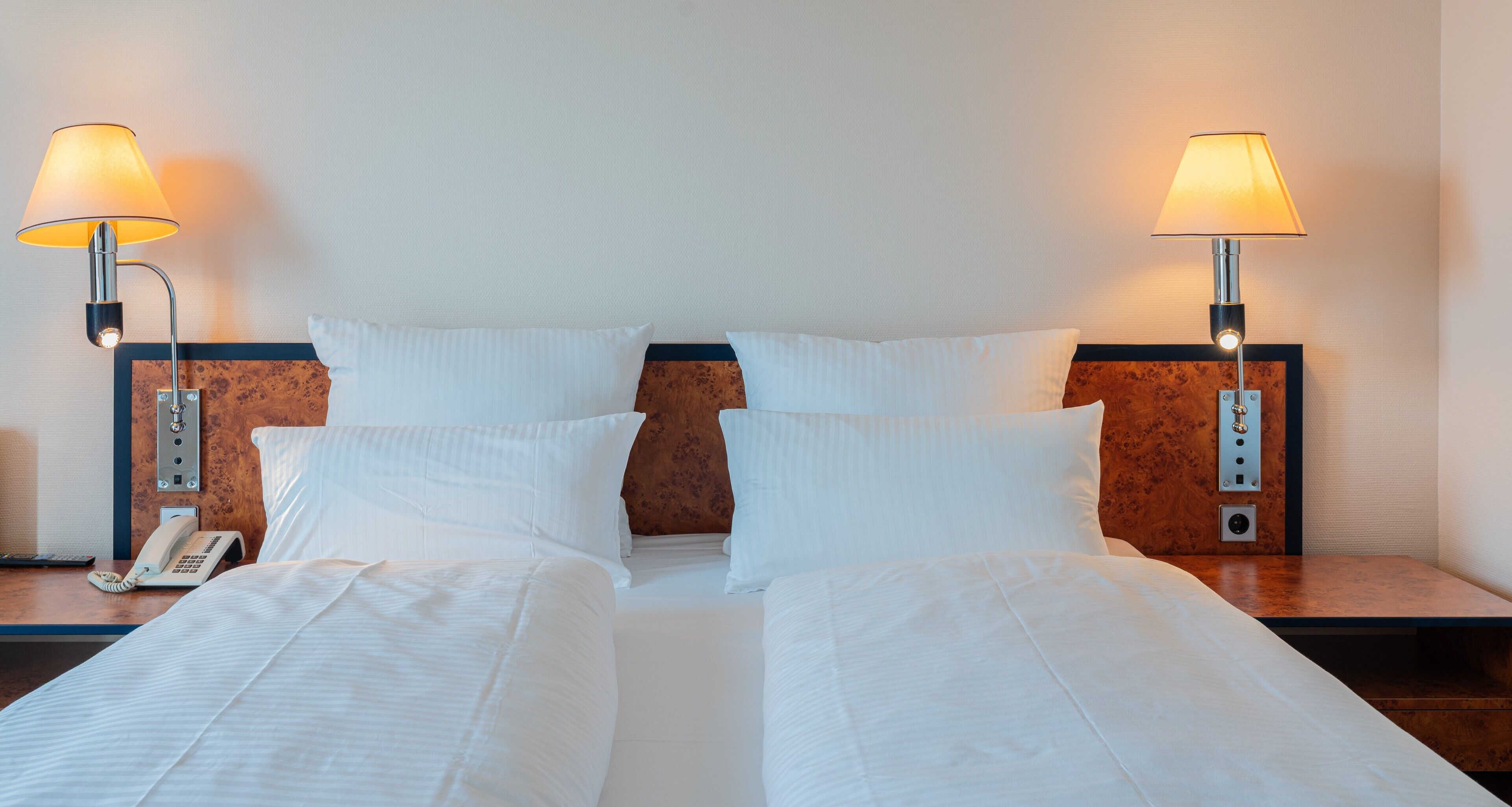 Habitación de hotel con cama doble, dos lámparas de noche, teléfono y cabecera de madera.