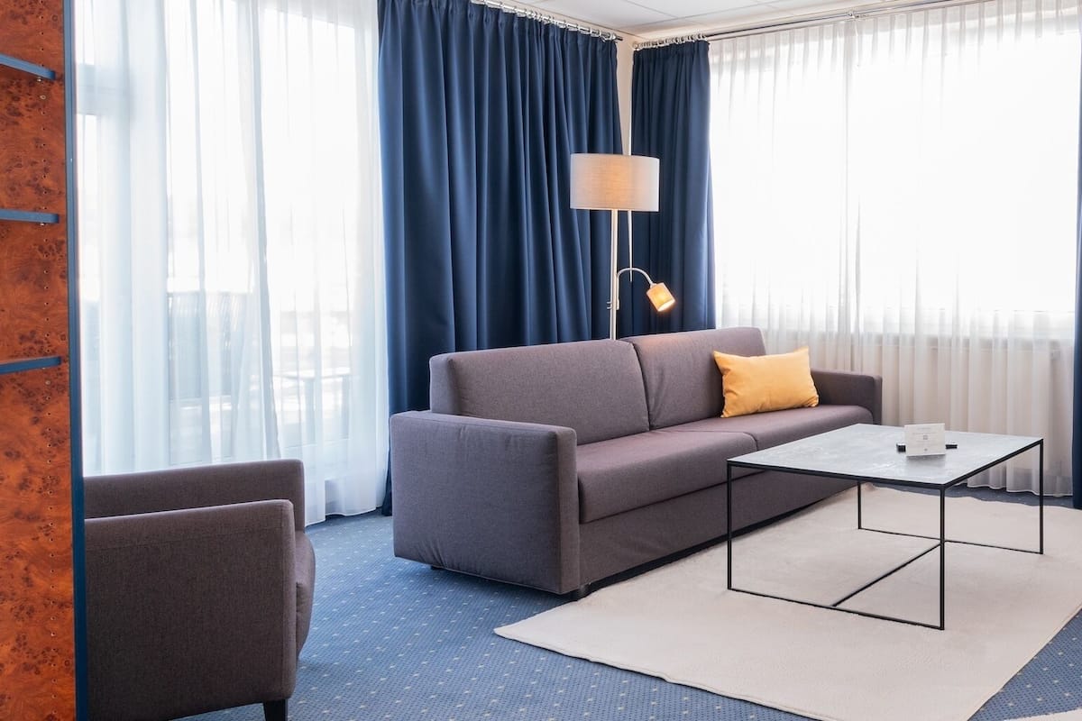 A hotel room with a sofa, a coffee table, a desk, a chair, a TV, and a wardrobe.