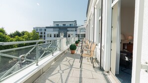 Een balkon met glazen hekwerk, bloempotten en buitenmeubilair.