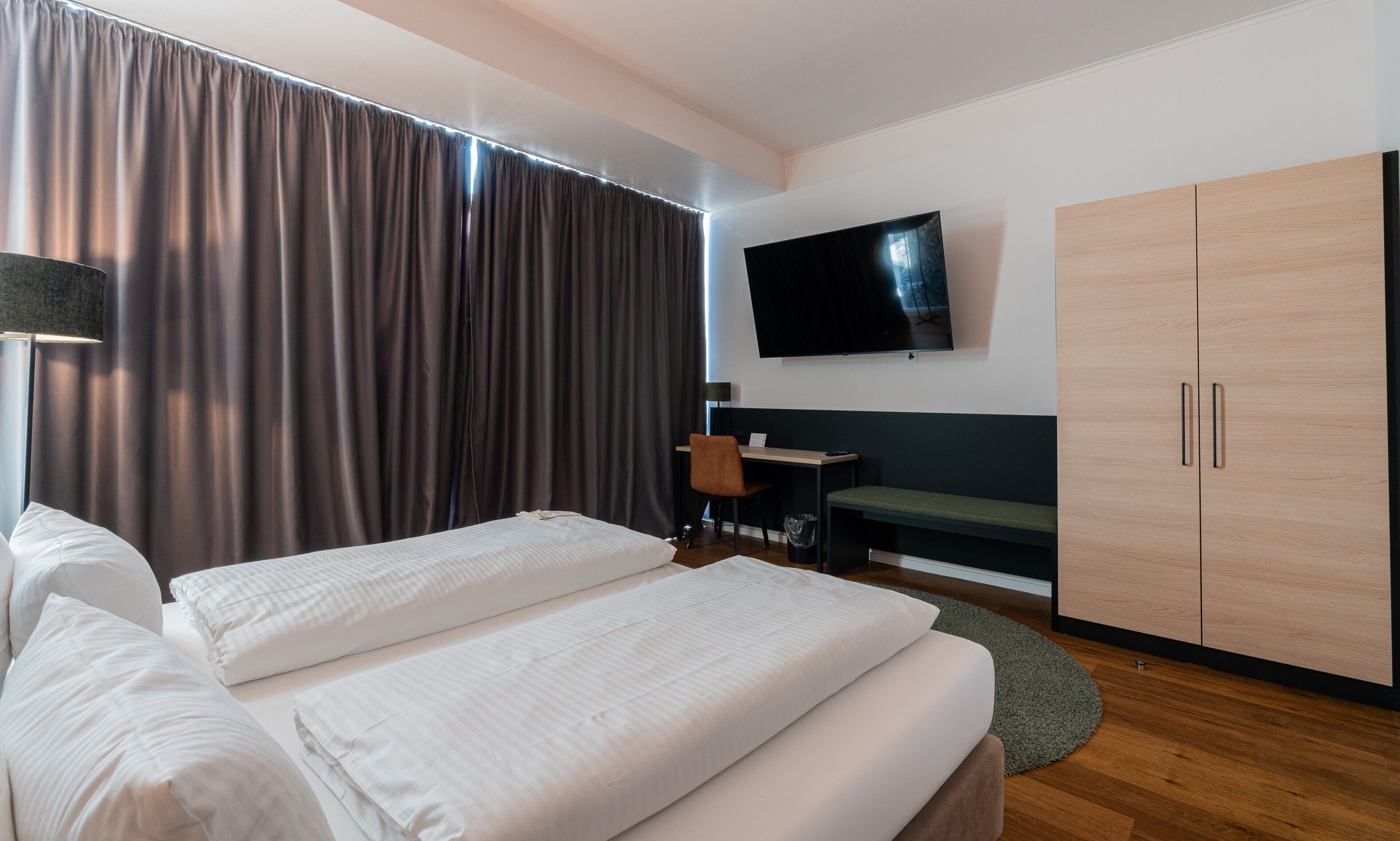 A hotel room with a bed, a desk, a chair, a TV, and a wardrobe.