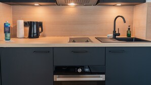 Een moderne keuken met een ingebouwde vaatwasser, een koffiezetapparaat, een waterkoker en een spoelbak met zeepdispenser.