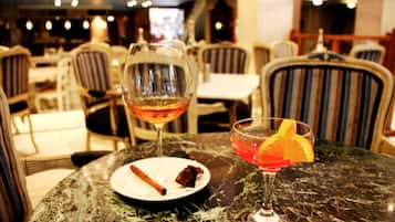Un ambiente de restaurante con una mesa de mármol, dos vasos de bebidas, un plato con una rodaja de naranja y una rama de canela.