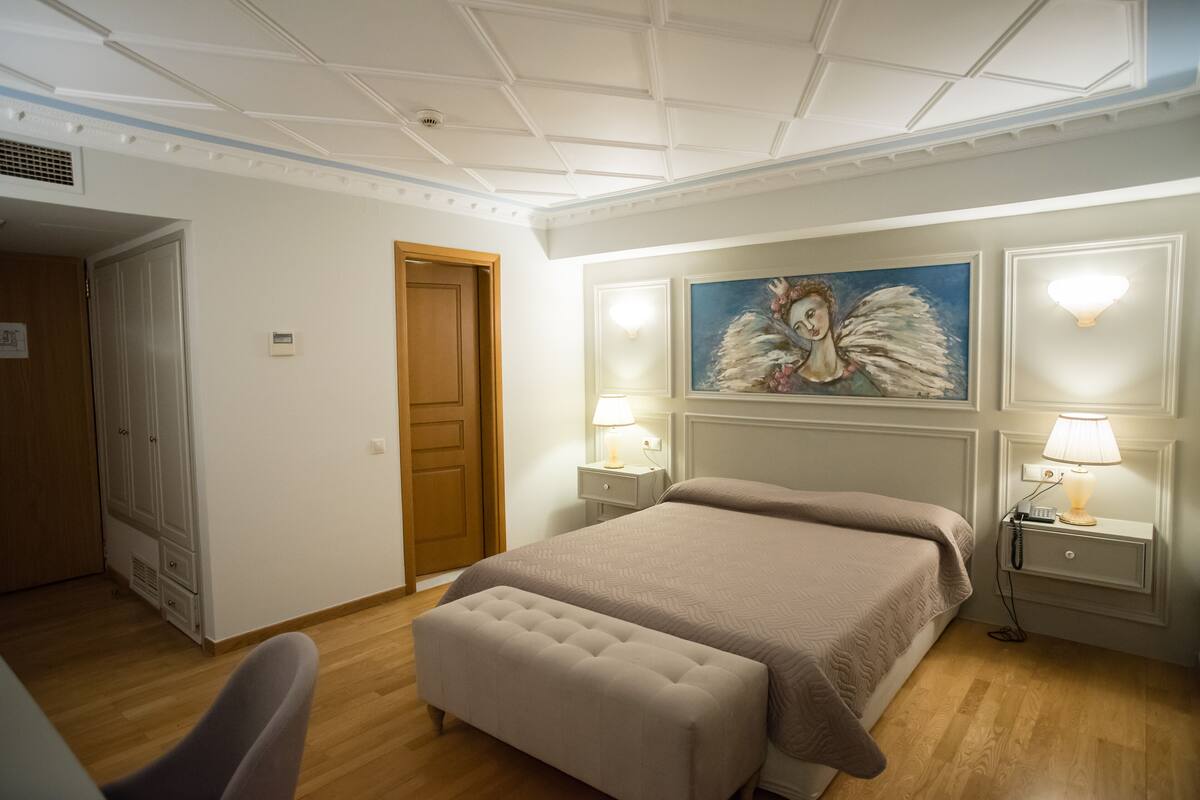 A hotel room with a large bed, a bench, a painting on the wall, and two bedside lamps.