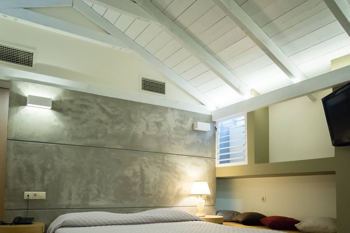 A bedroom with a bed, bedside table, lamp, and a TV mounted on the wall.