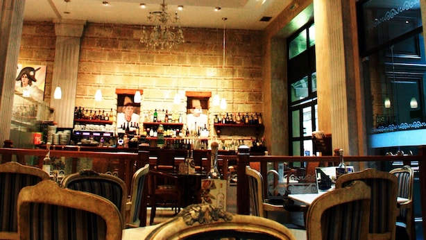 A bar area with a chandelier, wooden chairs, and a brick wall. - Byzantino Hotel Patras (Patras)