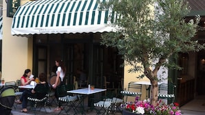 An outdoor cafe with striped awning, outdoor seating, and a potted plant with flowers. - Byzantino Hotel Patras (Patras)