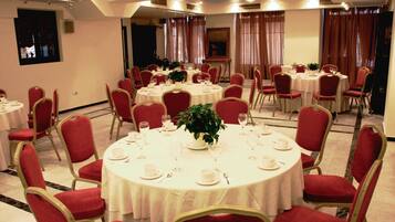 A banquet hall with multiple round tables, each set with white tablecloths, red chairs, and centerpieces.