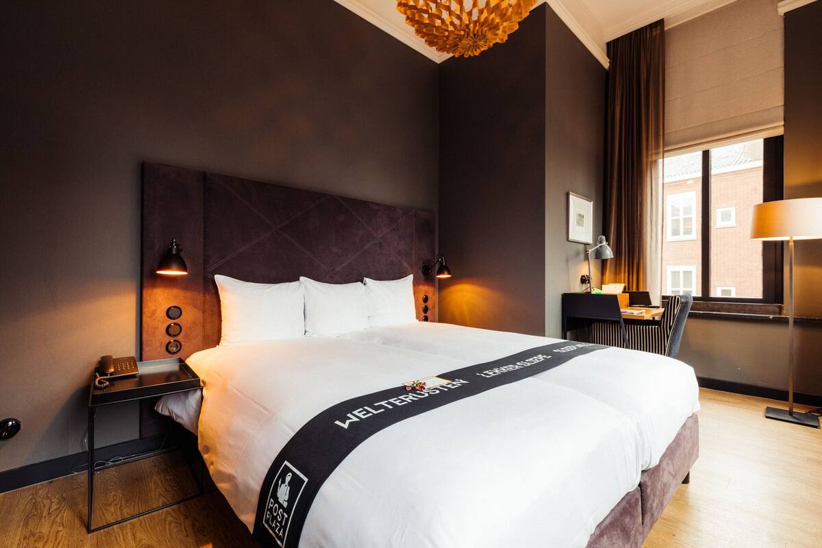 Ein Hotelzimmer mit einem großen Bett, einem Schreibtisch, einem Stuhl und einem Fenster mit Vorhängen.