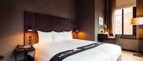 Habitación de hotel con una cama grande, un escritorio, una silla y una ventana con cortinas.