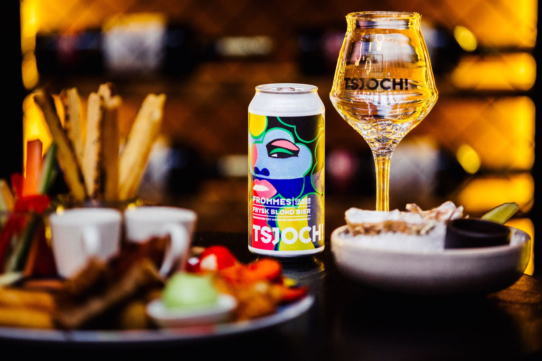 A can of TSOCH beer, a glass of beer, and a plate of food on a table.