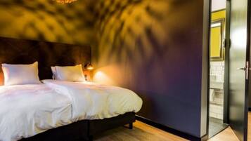 A bedroom with a bed, a headboard, a wall-mounted light, and a door leading to a bathroom.