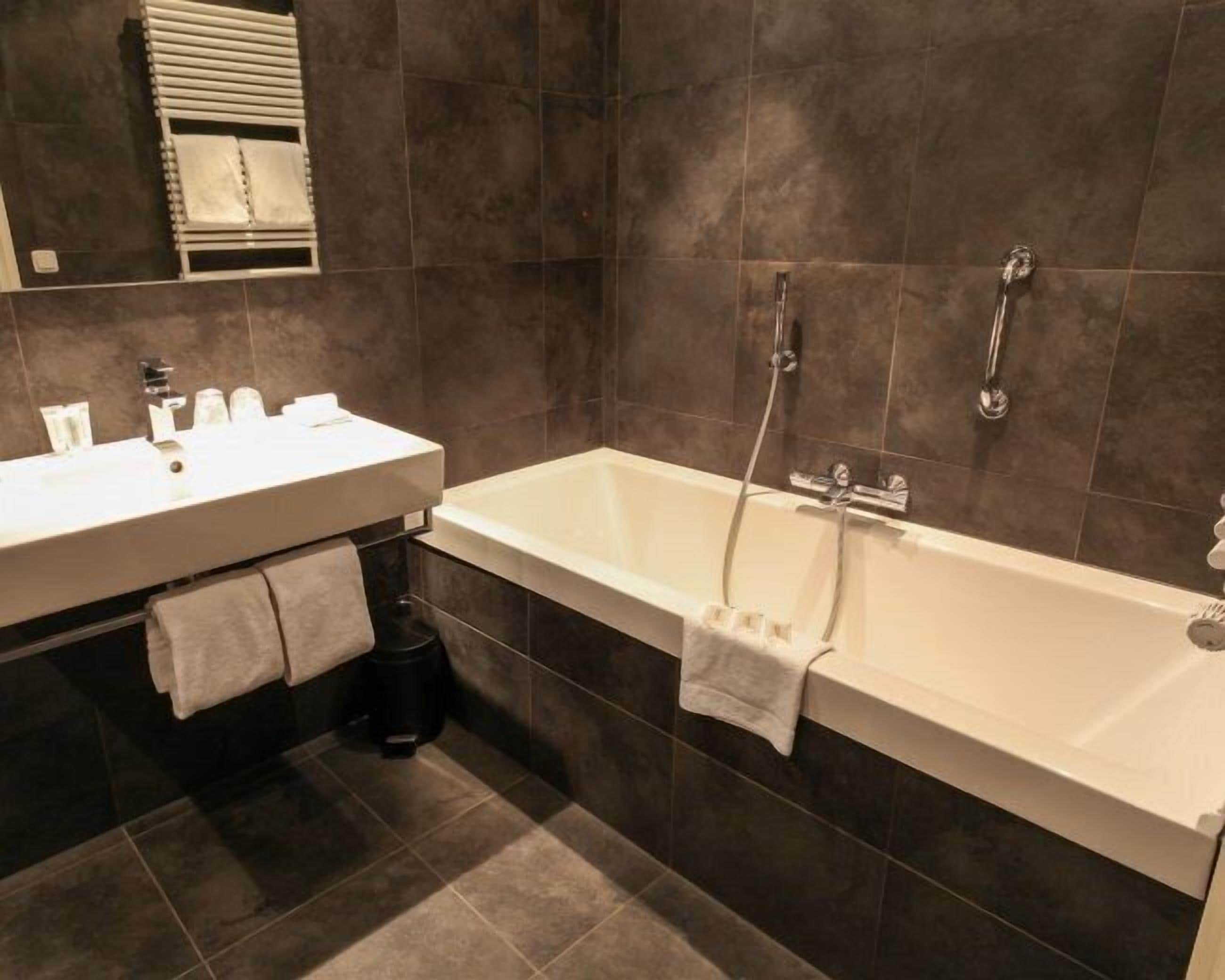 A modern bathroom with a white bathtub, a sink, and a mirror.