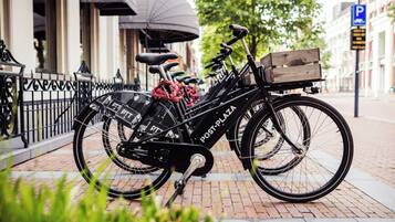 A black Post-PLAZA bicycle parked on a brick sidewalk with a wooden crate on the back.