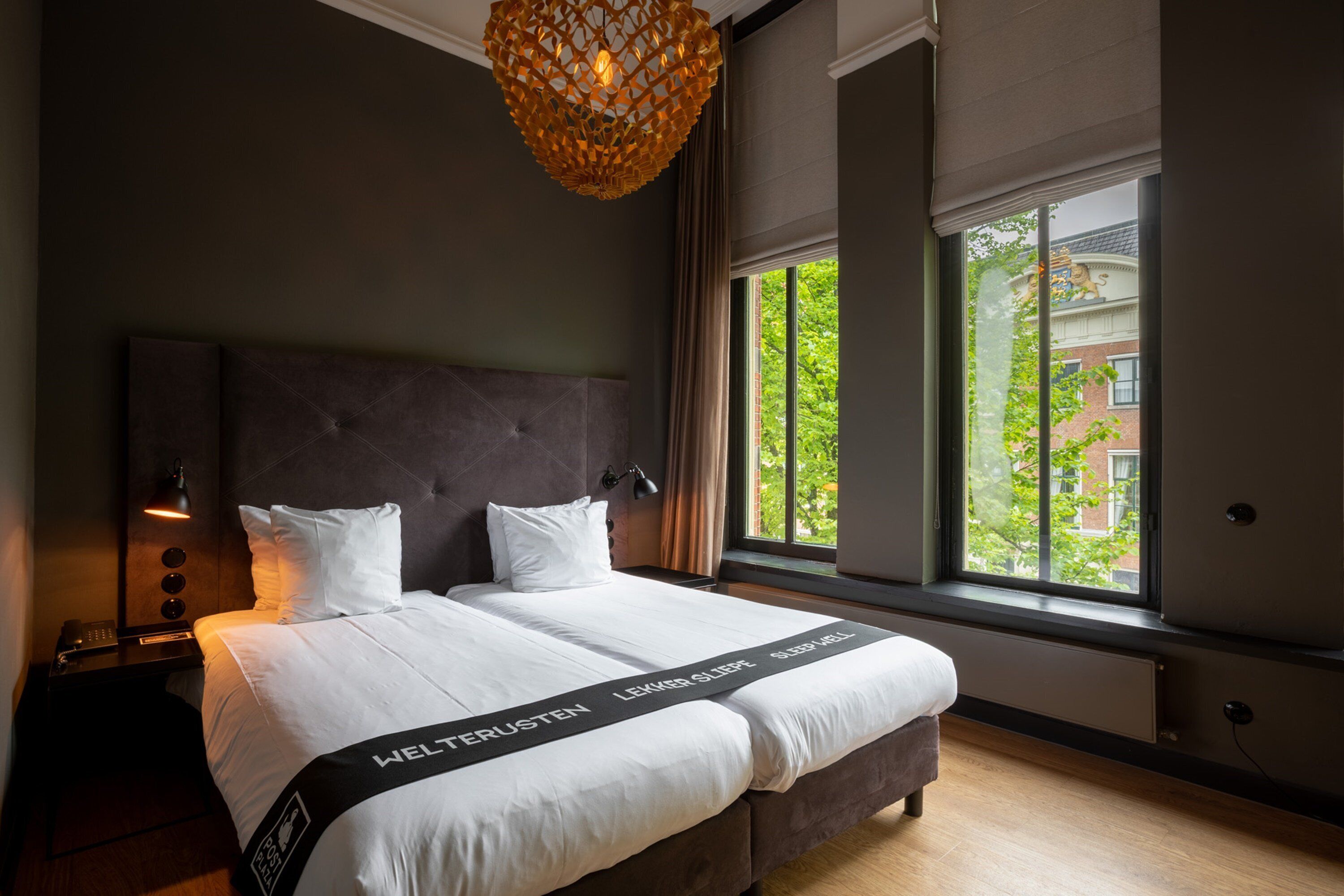 Habitación de hotel moderna con una cama grande, una mesita de noche, una lámpara y vistas a zonas verdes.