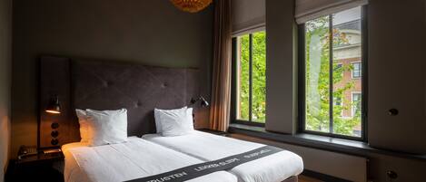 Habitación de hotel moderna con una cama grande, una mesita de noche, una lámpara y vistas a zonas verdes.