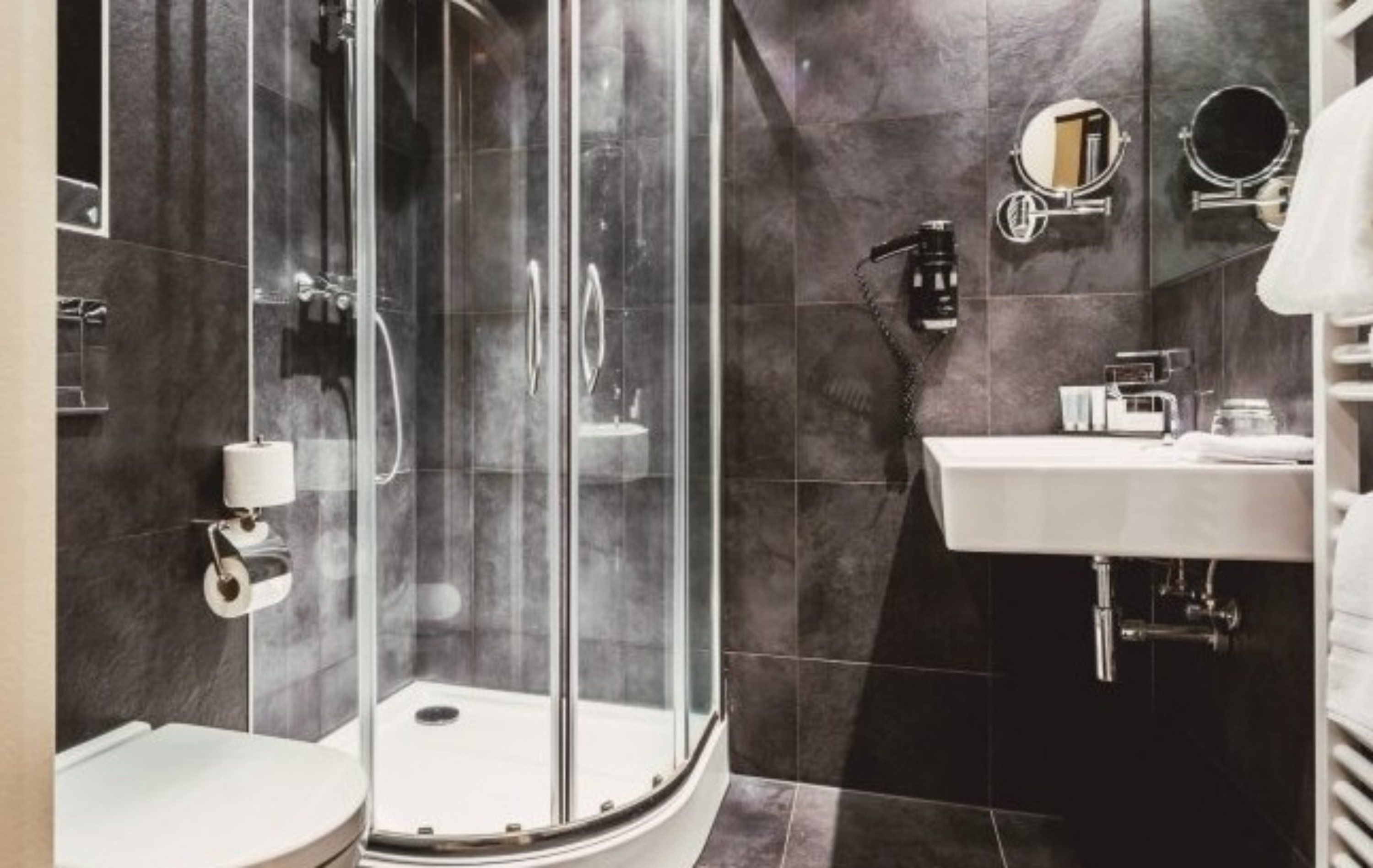 Ein modernes Badezimmer mit einer gläsernen Duschkabine, einem weißen Waschbecken und einem Spiegel.