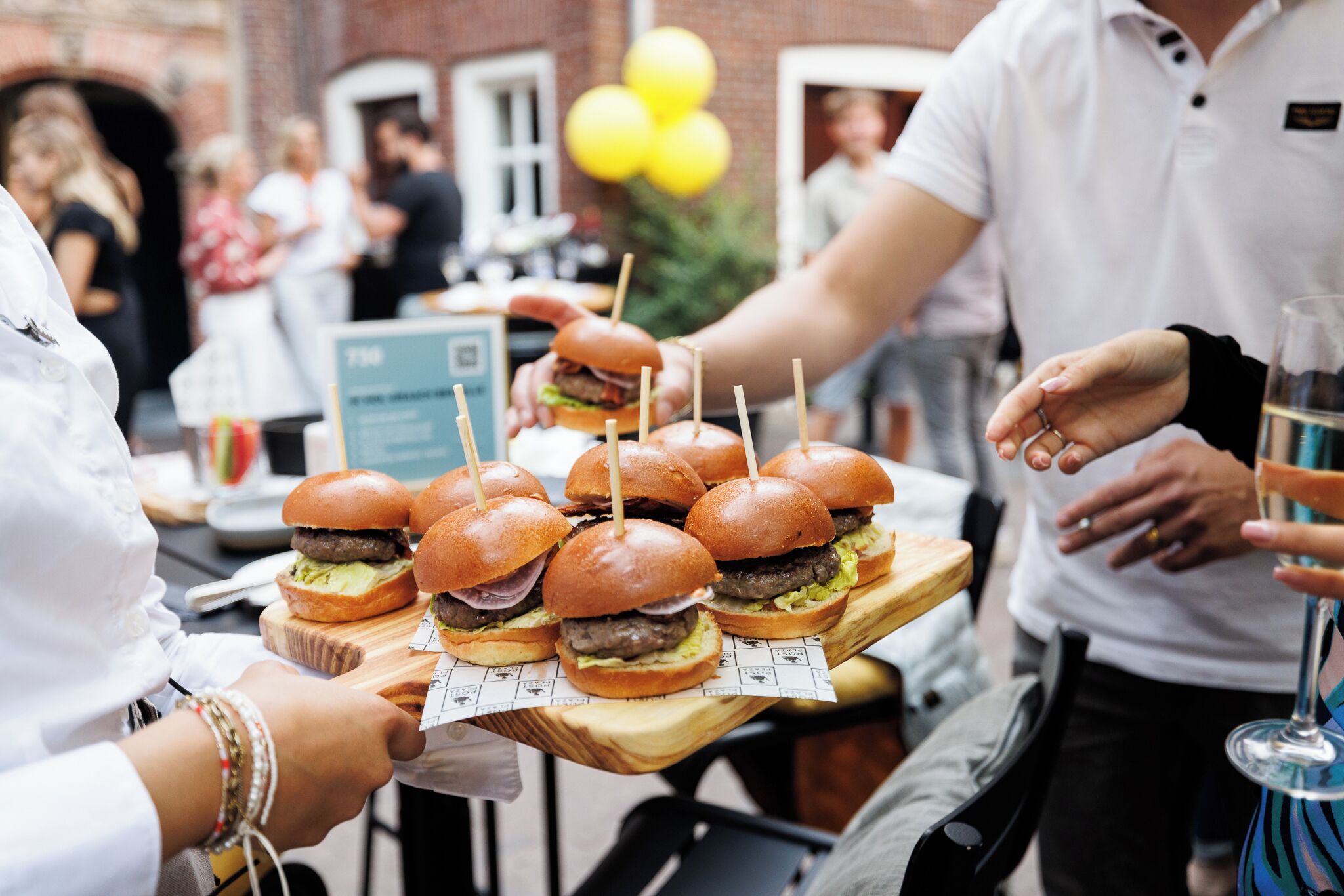 Een houten serveerplank met verschillende burgers, elk vastgeprikt met een cocktailprikker.