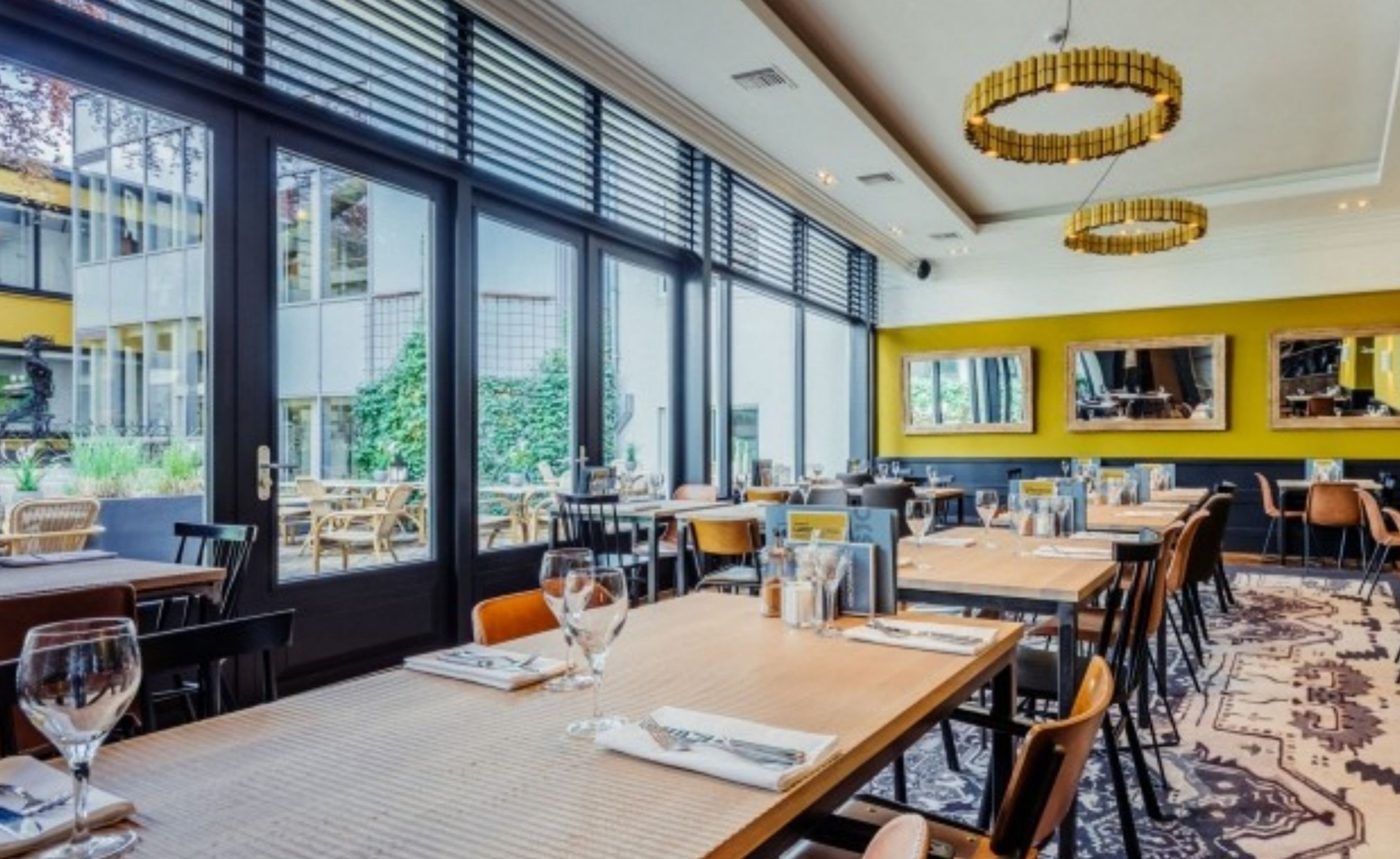 A modern restaurant with large windows, wooden tables, and yellow walls.
