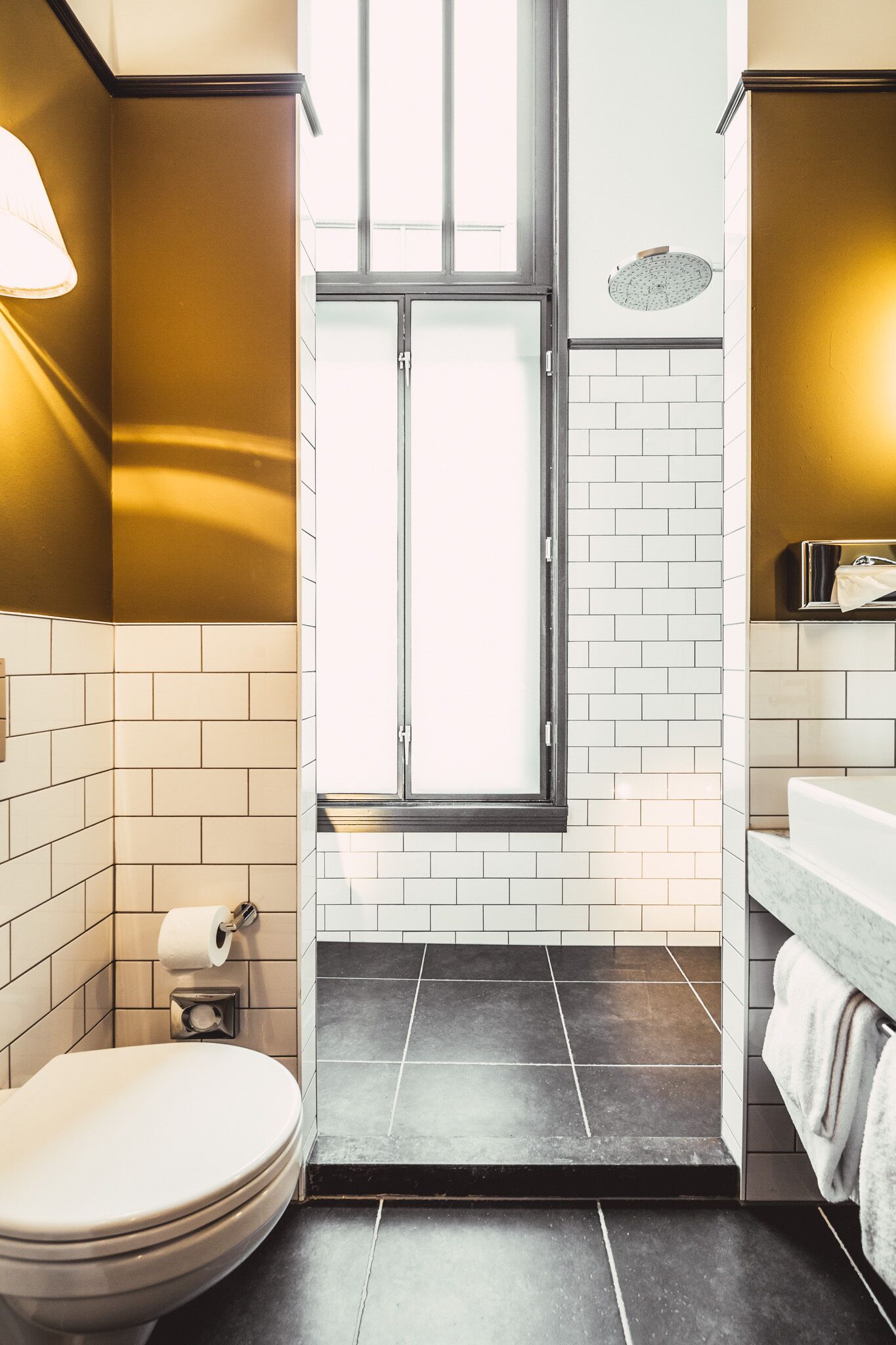 A modern bathroom with a toilet, a towel rack, a window, and a shower area.