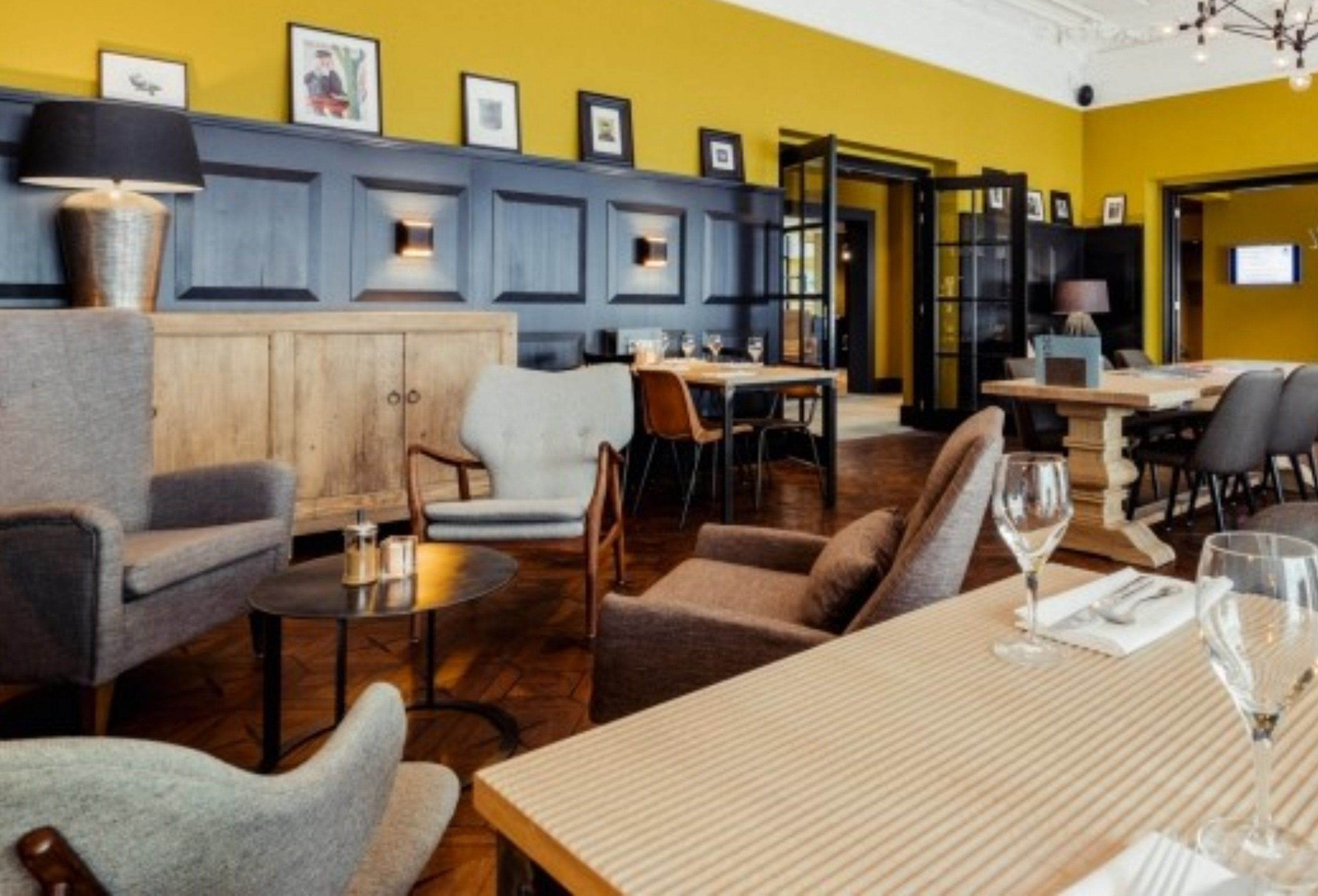 Un comedor con mesas y sillas de madera, una pared azul decorativa y cuadros sobre el mostrador.