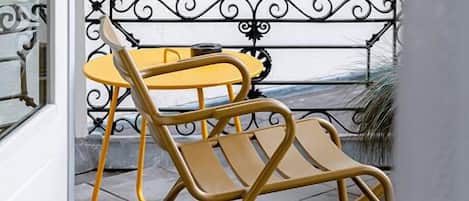 A yellow rocking chair outside a building with a white wall and a black wrought iron railing.