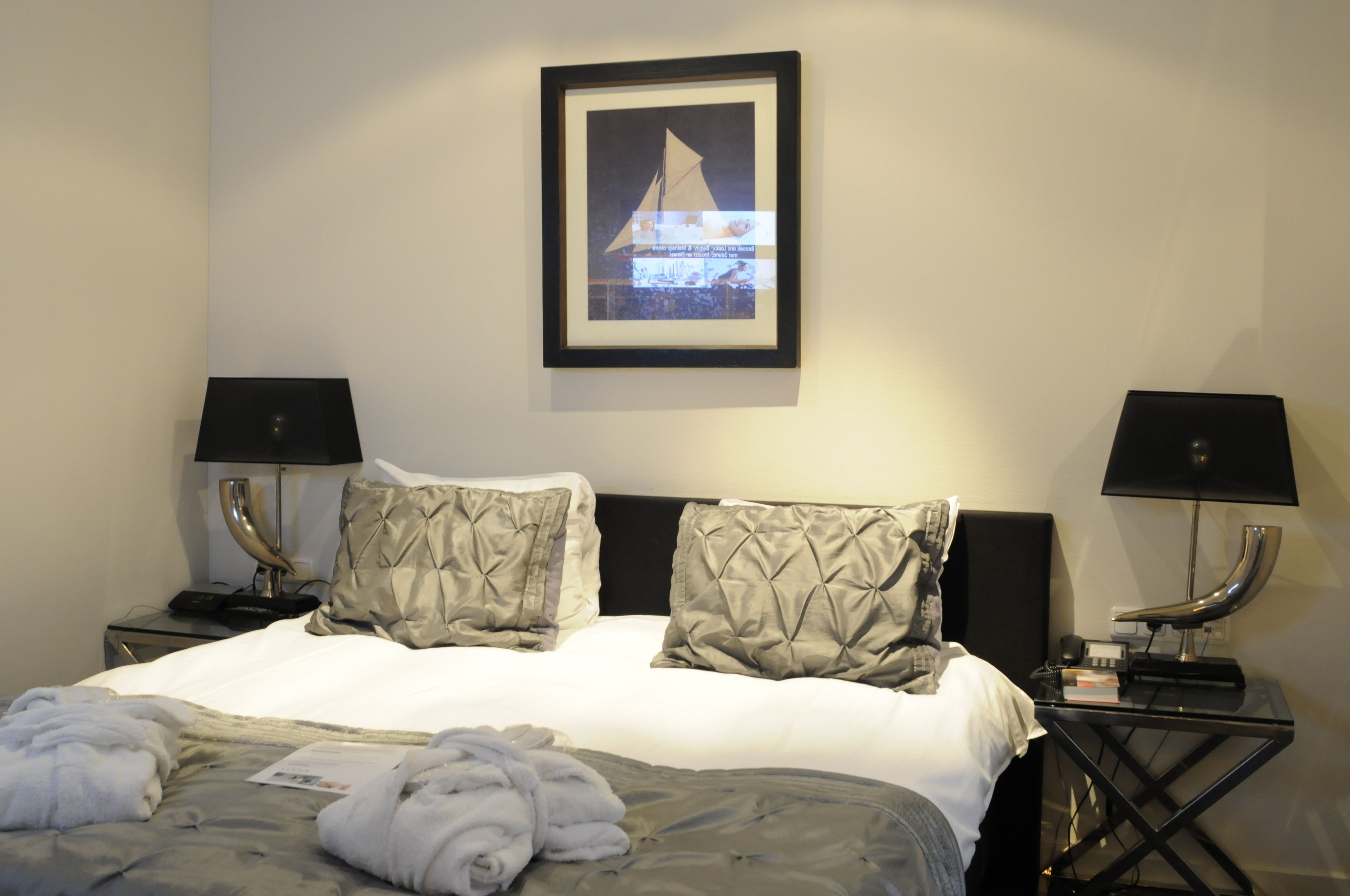 Une chambre d’hôtel avec un lit bien fait, deux tables de chevet avec des lampes, un tableau encadré au mur et une fenêtre donnant sur un beau paysage.