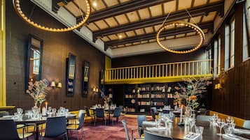 Un comedor con mesas dispuestas para el servicio, una estantería y una escalera que sube a un nivel superior.