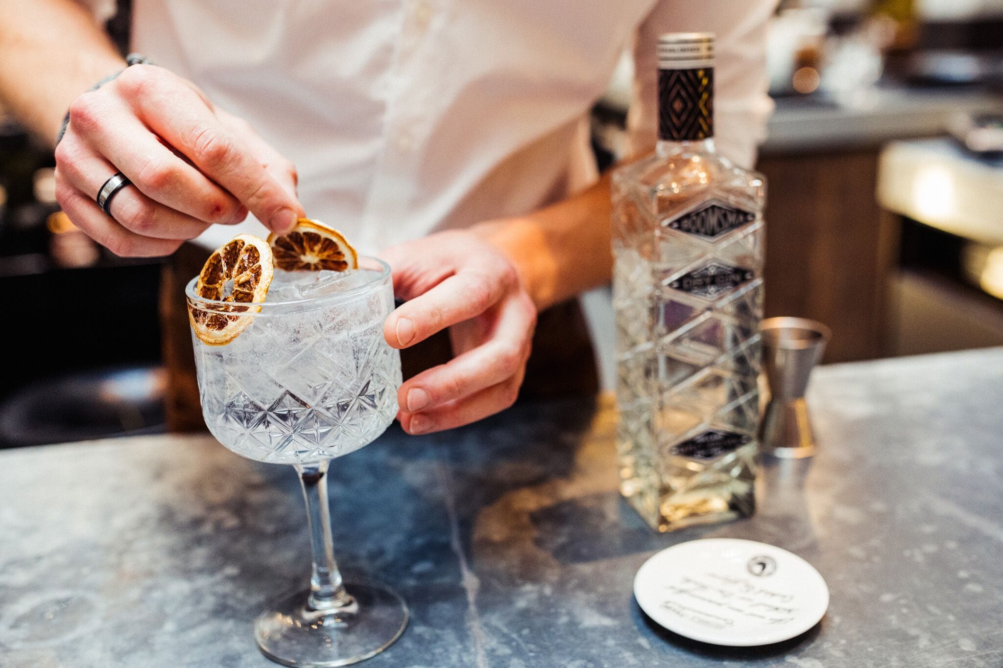 A person preparing a drink with a glass and a bottle on a marble countertop.