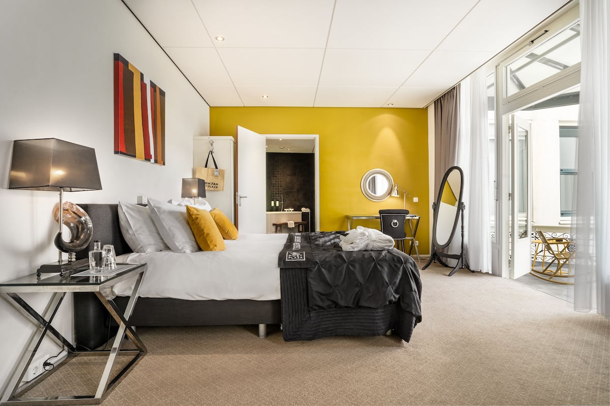 Ein modernes Hotelzimmer mit Bett, Nachttisch, Lampe und Blick ins Freie.