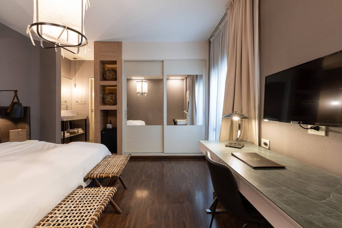 A hotel room with a bed, a desk, a TV, and a mirror.