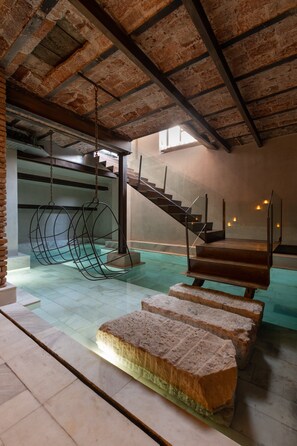 A spacious interior with a high ceiling, exposed brick walls, a staircase, and hanging chairs.