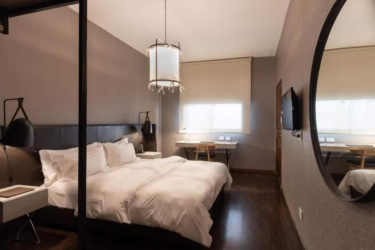 A modern hotel room with a large bed, bedside table, desk, chair, and a large mirror.