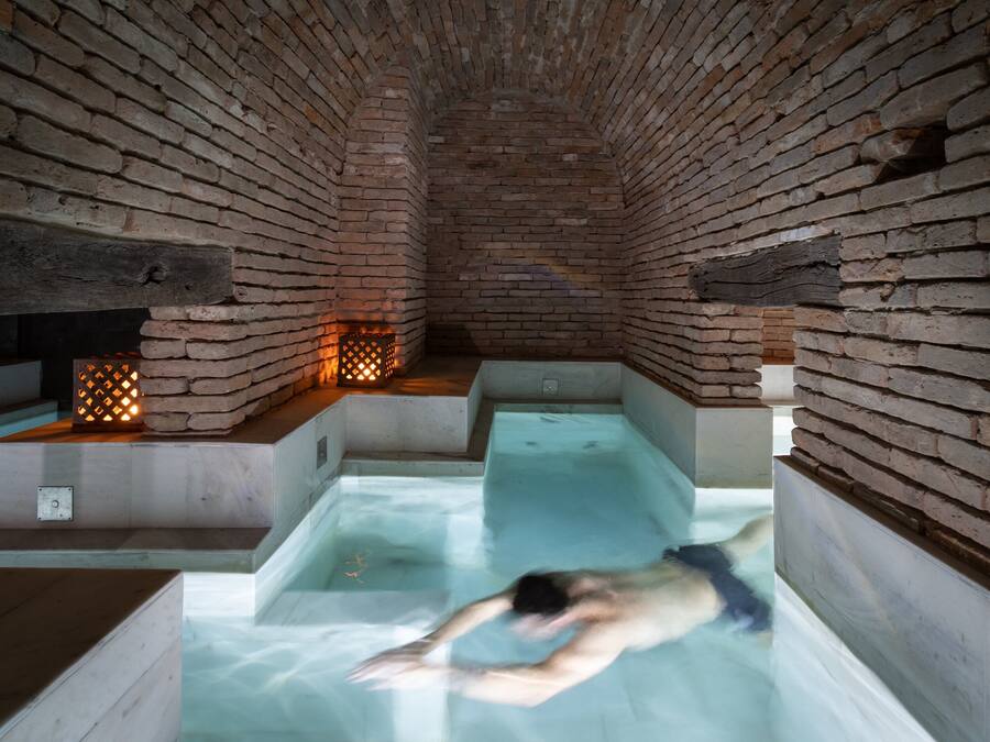 Un spa con paredes de ladrillo, una persona en una bañera y una pequeña zona de piscina.