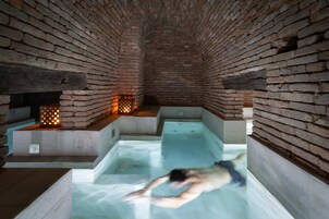 Un spa con paredes de ladrillo, una persona en una bañera y una pequeña zona de piscina.