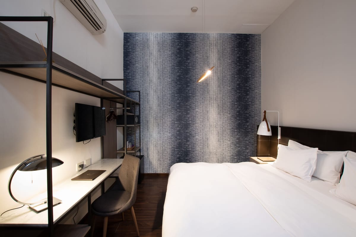 A hotel room with a bed, desk, chair, and a wall with a textured pattern.