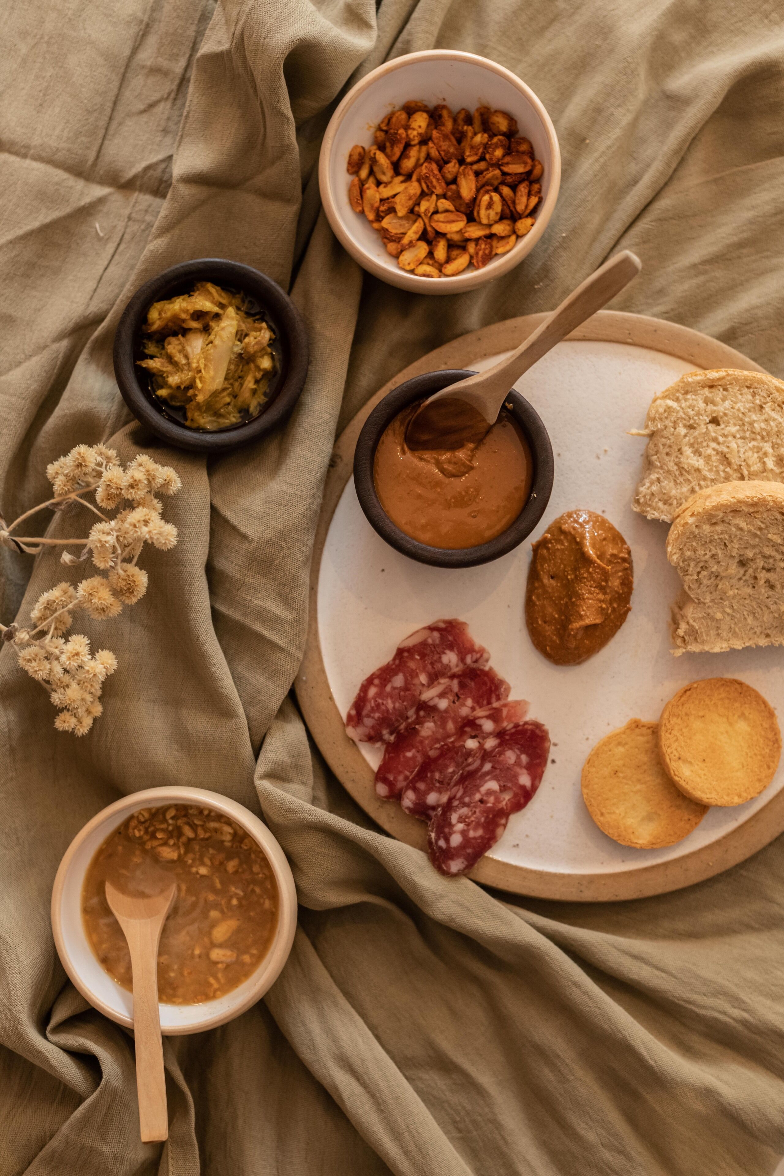 Un plato con diversos alimentos, como pan, galletas y una crema, sobre una superficie cubierta con tela.