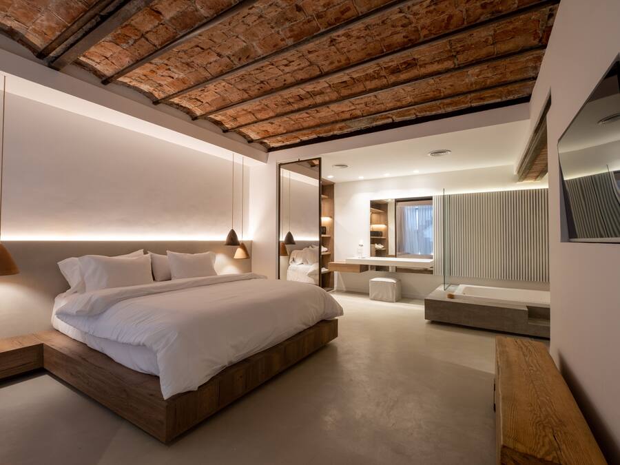 Quarto moderno com cama de madeira, um espelho grande e um banco embutido.