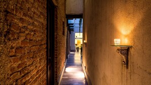 A narrow corridor with a wooden floor, brick walls, and a lit wall-mounted fixture. - Azur Real Hotel Boutique & Spa (Córdoba)