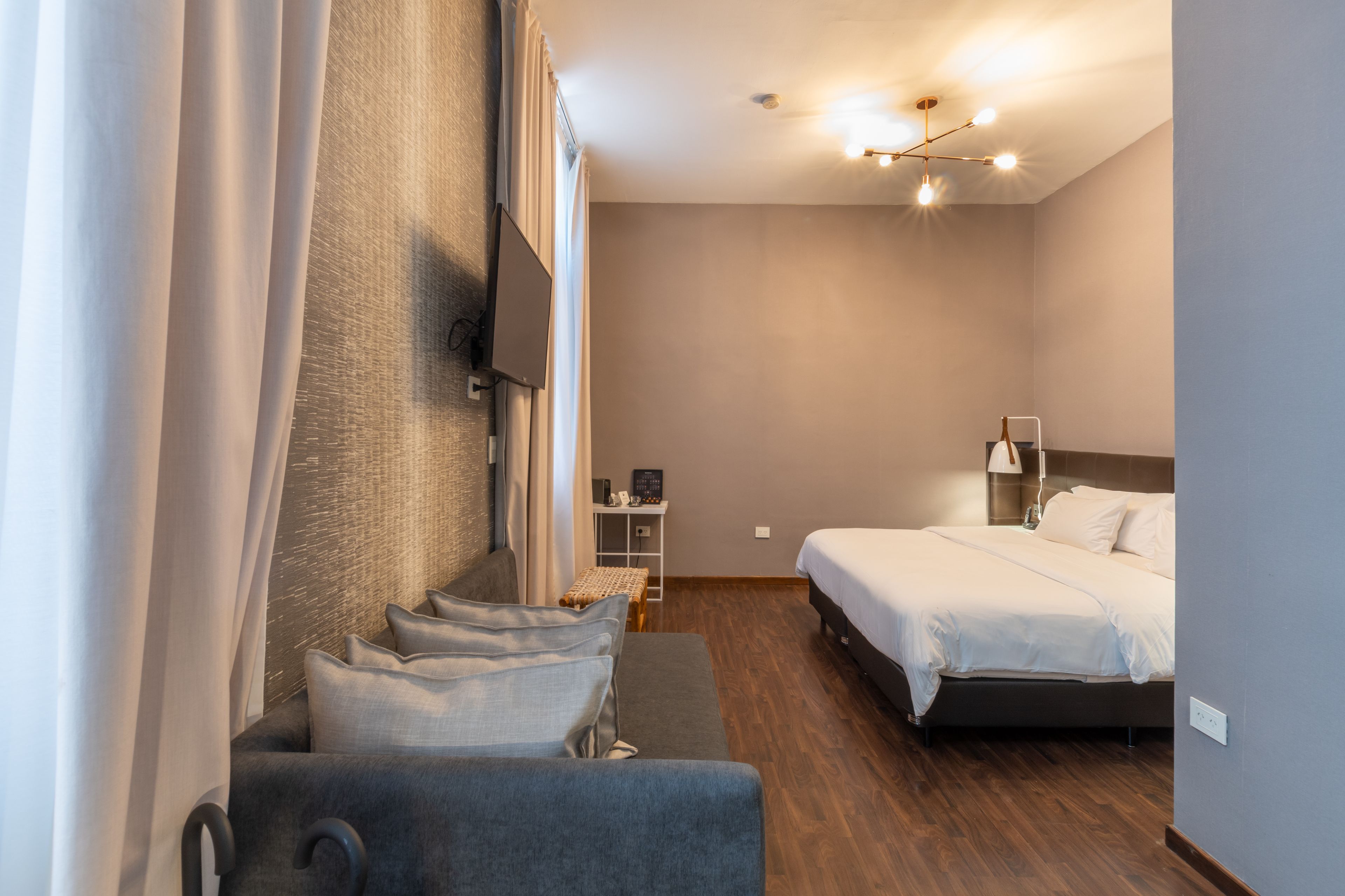 Ett modernt hotellrum med en soffa, en säng, en tv som är monterad på väggen och ett litet bord med en lampa.