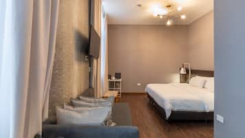 Ett modernt hotellrum med en soffa, en säng, en tv som är monterad på väggen och ett litet bord med en lampa.